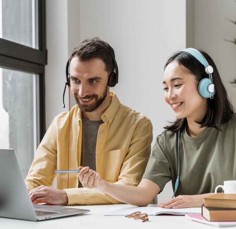 Couple wearing headphones attending online class together at shared workspace