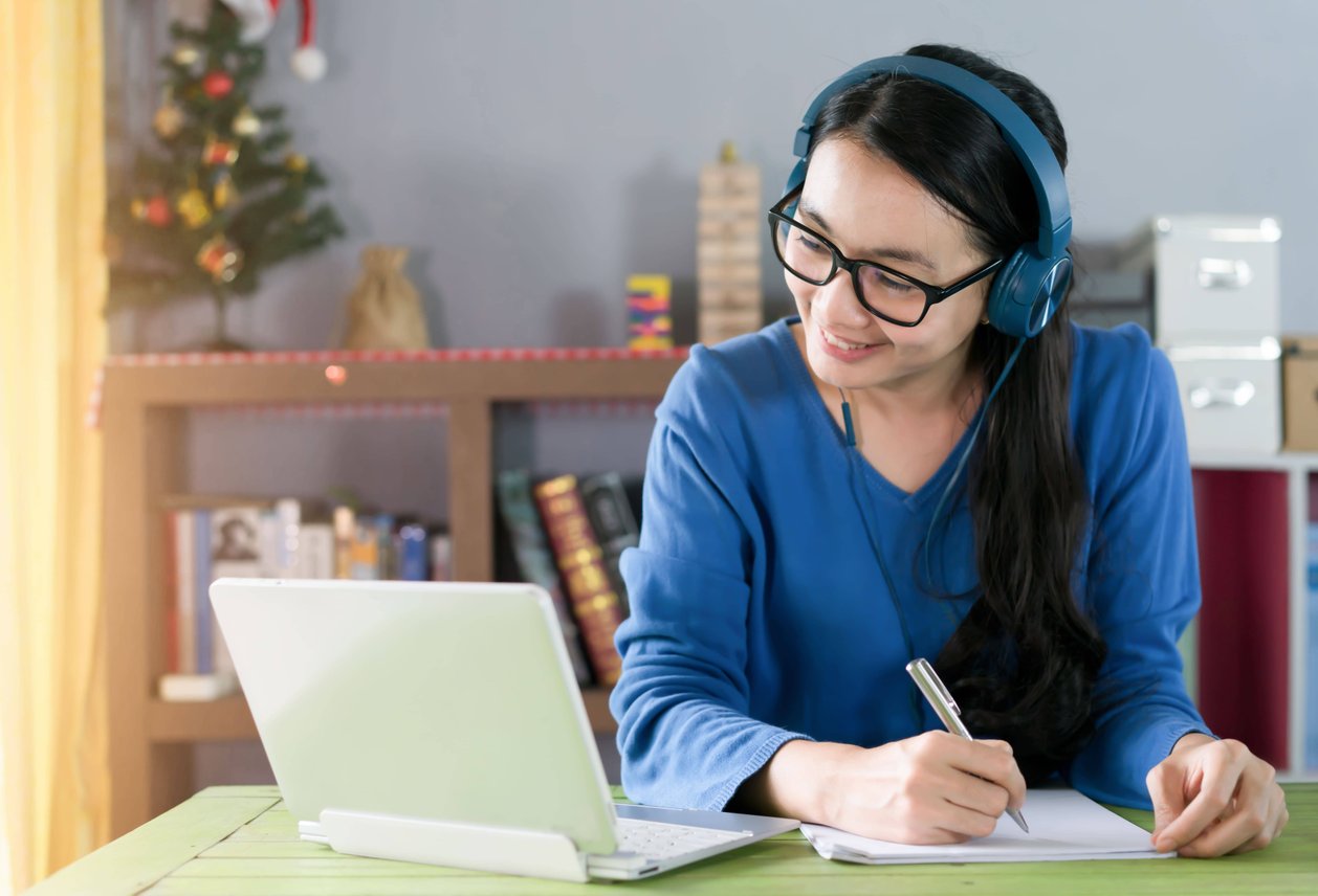 Woman with headphones taking notes during online learning session at home